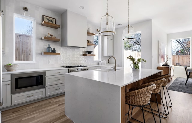 kitchen featuring sink, light hardwood / wood-style flooring, black microwave, a center island with sink, and pendant lighting