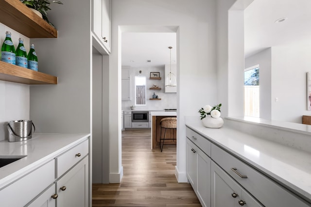 bar with white cabinets, light hardwood / wood-style flooring, hanging light fixtures, and built in microwave