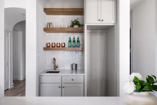 bar with light wood-type flooring, backsplash, white cabinetry, and sink