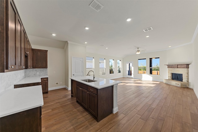 kitchen with a kitchen island with sink, a stone fireplace, sink, ceiling fan, and wood-type flooring