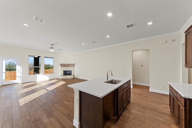 kitchen featuring ornamental molding, ceiling fan, sink, a center island with sink, and a stone fireplace