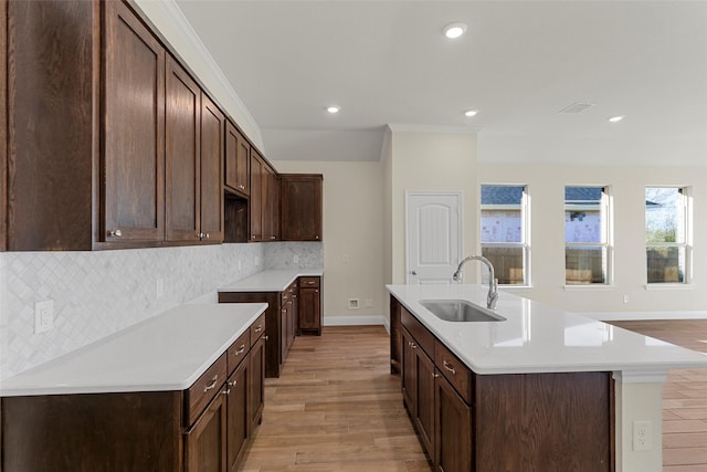 kitchen with dark brown cabinetry, tasteful backsplash, a kitchen island with sink, and sink