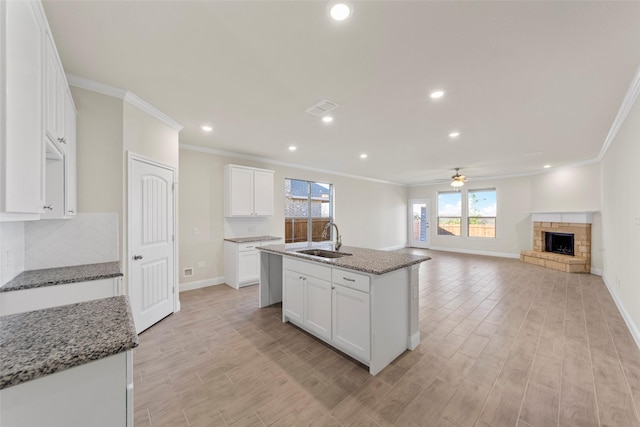 kitchen with stone counters, white cabinetry, sink, and a center island with sink