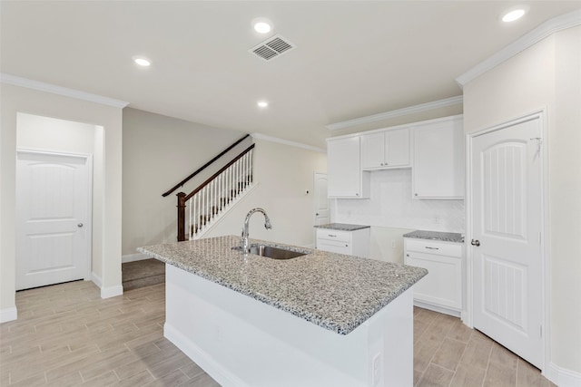 kitchen with white cabinets, a center island with sink, light stone counters, and sink