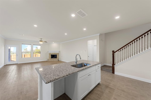 kitchen with a kitchen island with sink, sink, white cabinets, and light stone counters