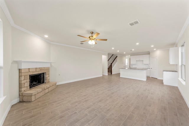 unfurnished living room featuring crown molding, ceiling fan, a stone fireplace, and light hardwood / wood-style flooring