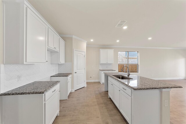 kitchen featuring white cabinets, dark stone countertops, sink, and a kitchen island with sink