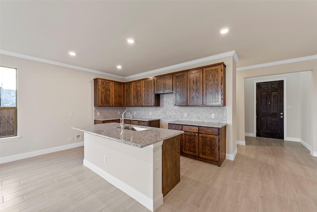 kitchen with a center island with sink, light stone counters, ornamental molding, and sink