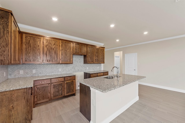 kitchen with light stone counters, crown molding, sink, and a kitchen island with sink