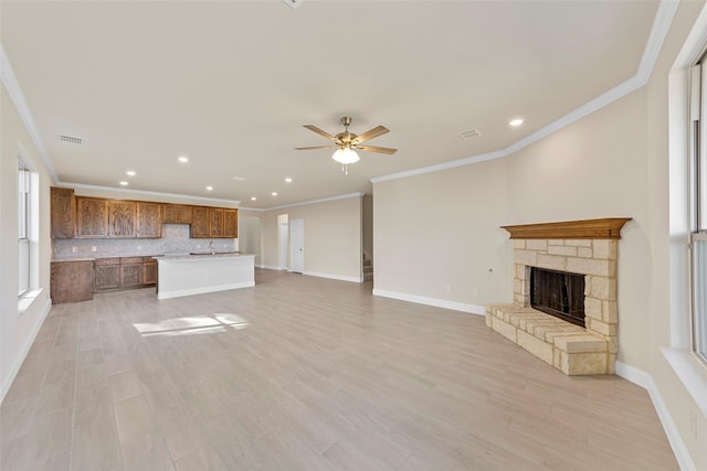 unfurnished living room featuring crown molding, ceiling fan, a stone fireplace, and light hardwood / wood-style flooring