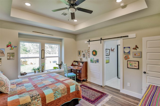 bedroom featuring ceiling fan, a barn door, a raised ceiling, and light wood-type flooring