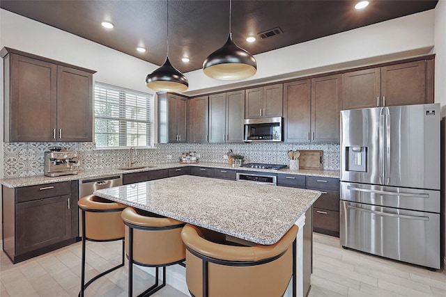 kitchen with light stone countertops, a kitchen island, hanging light fixtures, and appliances with stainless steel finishes