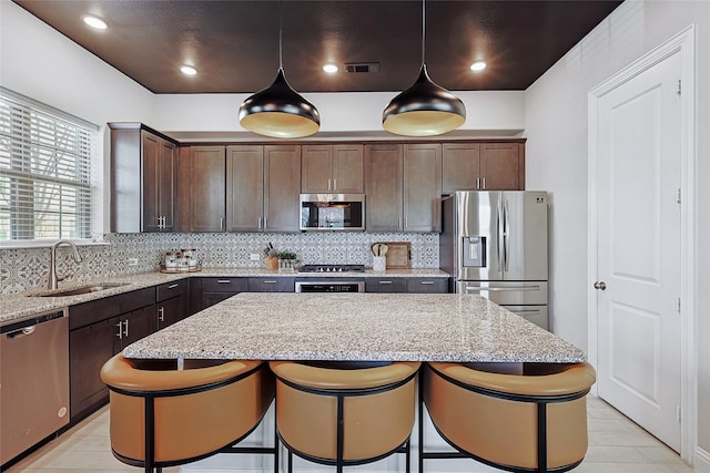 kitchen featuring a kitchen island, pendant lighting, light stone counters, and appliances with stainless steel finishes