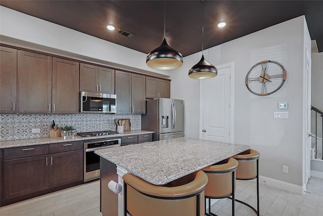 kitchen featuring light stone countertops, pendant lighting, stainless steel appliances, tasteful backsplash, and dark brown cabinetry