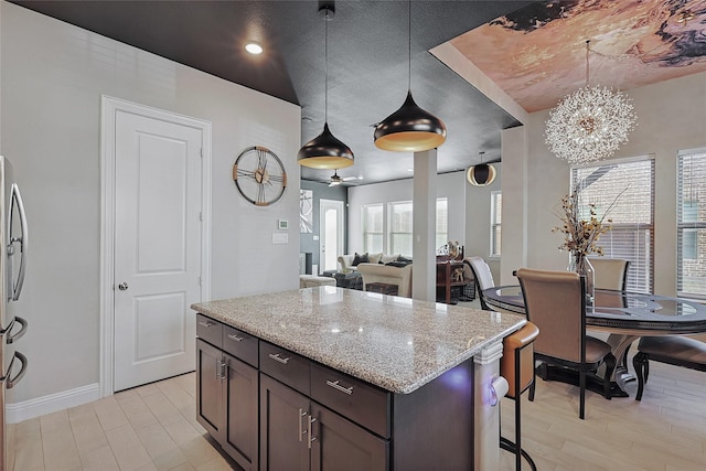 kitchen featuring decorative light fixtures, light stone counters, dark brown cabinets, and a center island