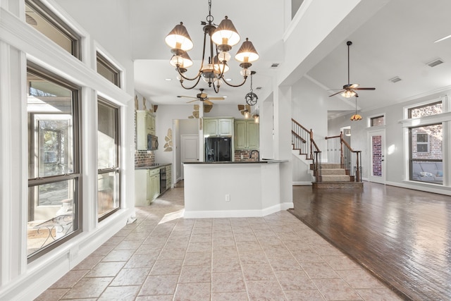 kitchen with green cabinets, black refrigerator with ice dispenser, kitchen peninsula, crown molding, and ceiling fan with notable chandelier