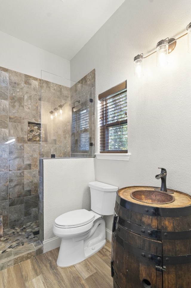 bathroom with hardwood / wood-style flooring, vanity, toilet, and a tile shower