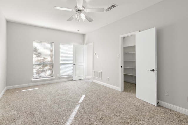 unfurnished bedroom with a walk in closet, ceiling fan, a closet, and light colored carpet