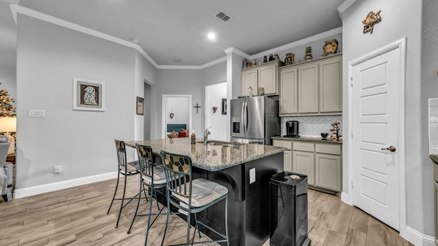 kitchen with sink, light stone counters, stainless steel fridge, an island with sink, and a kitchen bar