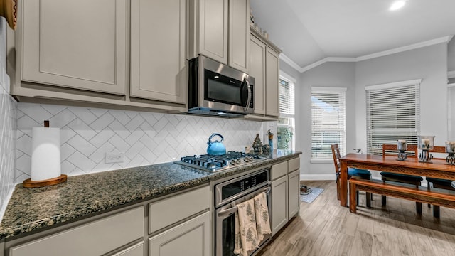 kitchen featuring backsplash, vaulted ceiling, ornamental molding, appliances with stainless steel finishes, and light hardwood / wood-style floors