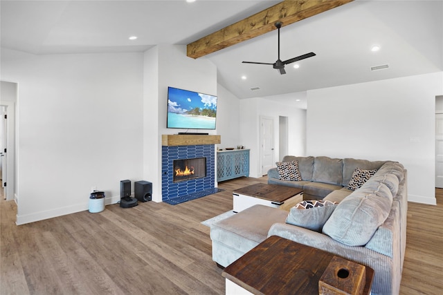 living room featuring a tiled fireplace, ceiling fan, hardwood / wood-style floors, and lofted ceiling with beams