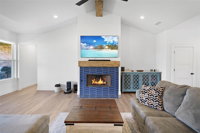 living room featuring a tiled fireplace, light hardwood / wood-style flooring, and lofted ceiling with beams