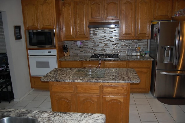 kitchen featuring brown cabinets, light tile patterned floors, stainless steel appliances, and ventilation hood