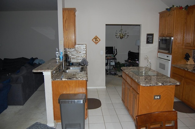 kitchen featuring white oven, built in microwave, brown cabinetry, a sink, and dark stone counters