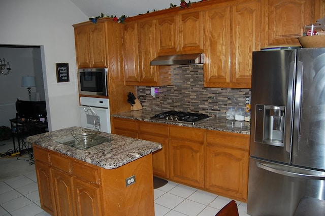 kitchen featuring dark stone counters, wall chimney exhaust hood, appliances with stainless steel finishes, and brown cabinetry