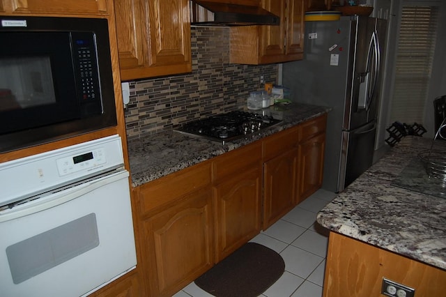 kitchen with stainless steel appliances, brown cabinets, wall chimney range hood, and decorative backsplash