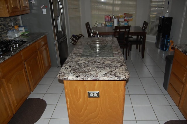 kitchen with light tile patterned floors, black gas stovetop, brown cabinetry, and an island with sink