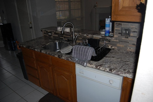 kitchen with tasteful backsplash, dishwasher, brown cabinets, a sink, and light tile patterned flooring