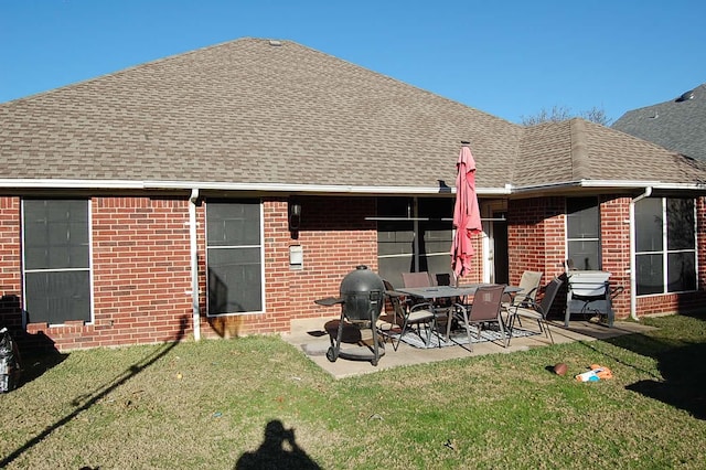 rear view of house featuring a shingled roof, a patio area, brick siding, and a yard