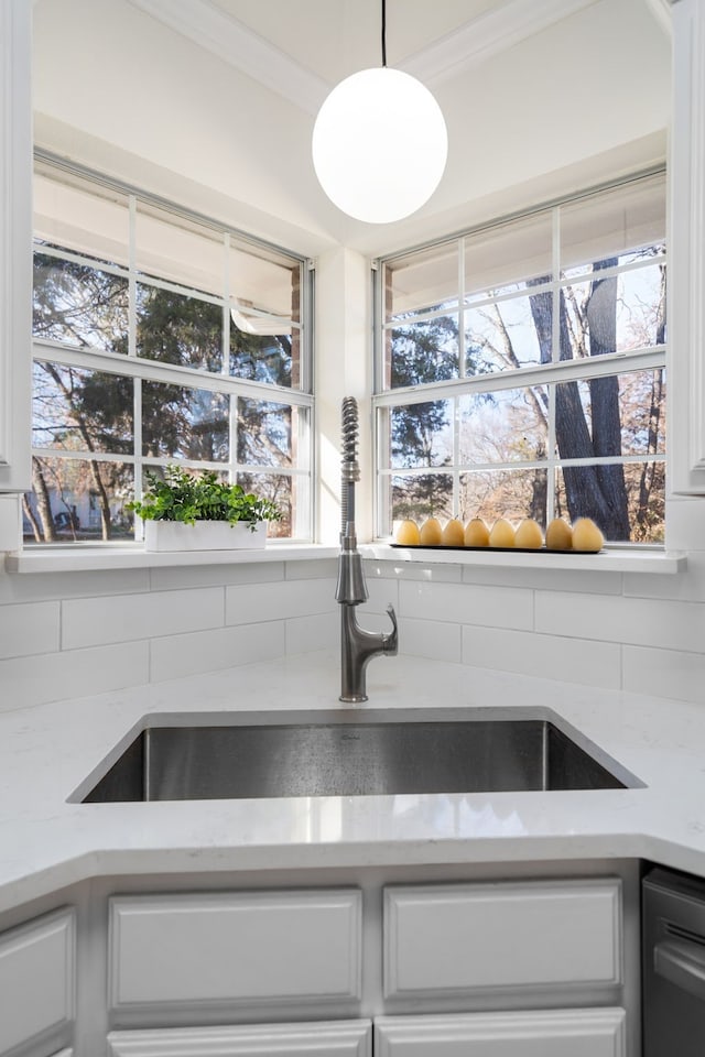 room details featuring light stone counters, ornamental molding, sink, white cabinets, and hanging light fixtures