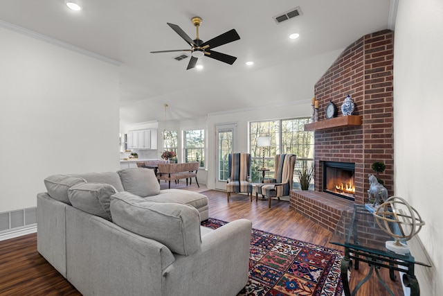 living room featuring ceiling fan, dark wood-type flooring, vaulted ceiling, a fireplace, and ornamental molding