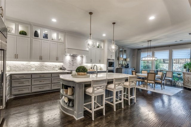 kitchen featuring hanging light fixtures, a center island with sink, white cabinets, and backsplash