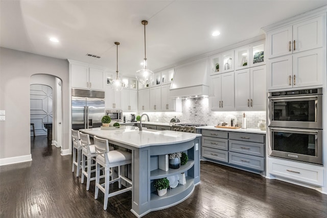 kitchen with hanging light fixtures, white cabinetry, custom range hood, and a center island with sink