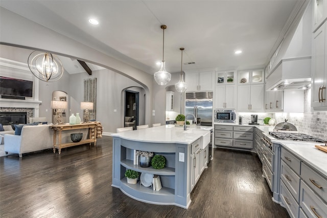 kitchen with pendant lighting, white cabinetry, built in appliances, a center island with sink, and custom exhaust hood