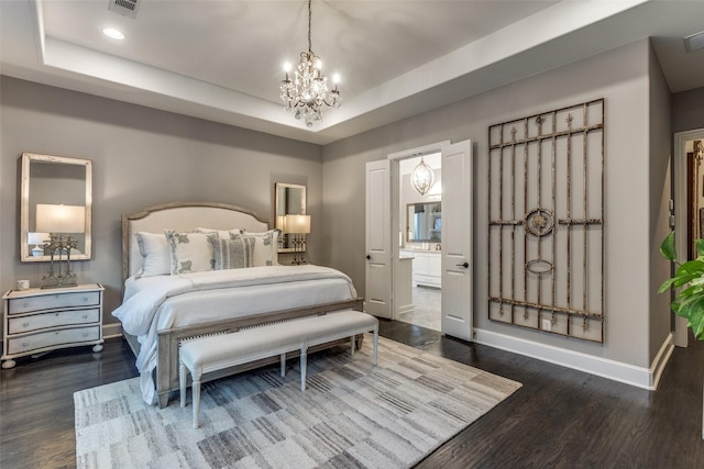 bedroom with dark hardwood / wood-style flooring, connected bathroom, a tray ceiling, and a chandelier