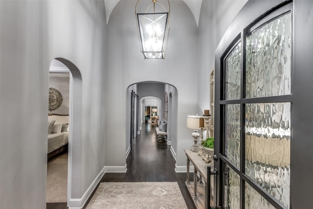 hallway with an inviting chandelier, a towering ceiling, and dark wood-type flooring