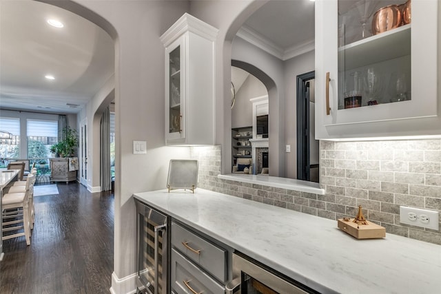 kitchen featuring crown molding, dark wood-type flooring, white cabinetry, light stone counters, and beverage cooler