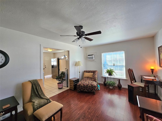 sitting room featuring a wall unit AC, ceiling fan with notable chandelier, a textured ceiling, and light wood-type flooring