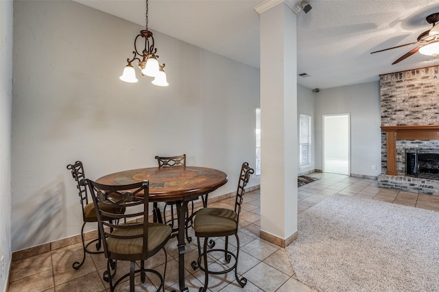 tiled dining space featuring a textured ceiling, a stone fireplace, and ceiling fan with notable chandelier