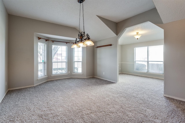 carpeted spare room featuring a notable chandelier, a healthy amount of sunlight, a textured ceiling, and vaulted ceiling