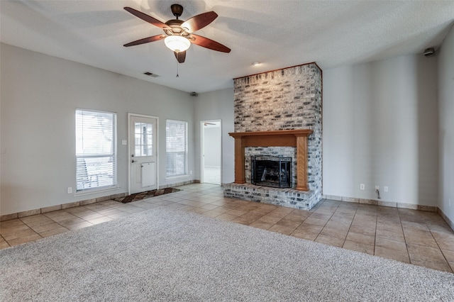 unfurnished living room with ceiling fan, a fireplace, light tile patterned floors, and a textured ceiling