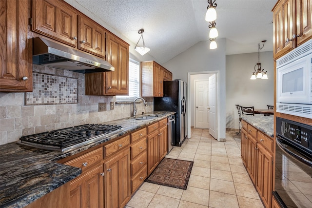 kitchen featuring sink, vaulted ceiling, dark stone countertops, decorative light fixtures, and stainless steel appliances