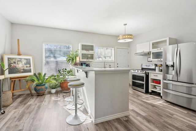 kitchen with light hardwood / wood-style floors, appliances with stainless steel finishes, white cabinets, kitchen peninsula, and a breakfast bar area