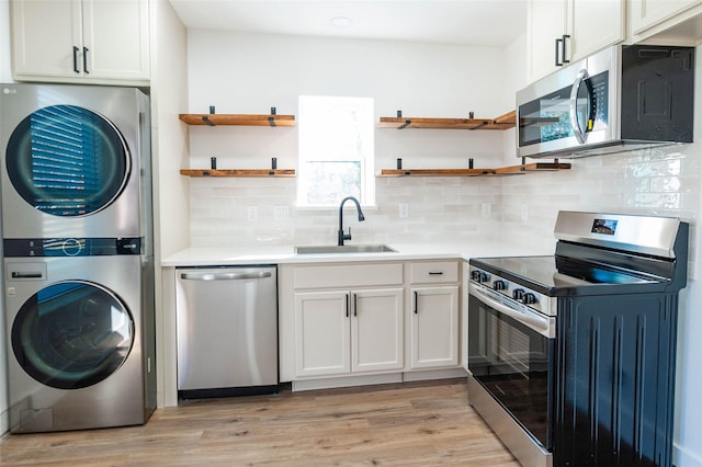 kitchen with white cabinetry, sink, stainless steel appliances, light hardwood / wood-style flooring, and stacked washer / drying machine