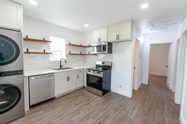 kitchen featuring sink, light wood-type flooring, appliances with stainless steel finishes, white cabinetry, and stacked washer / dryer