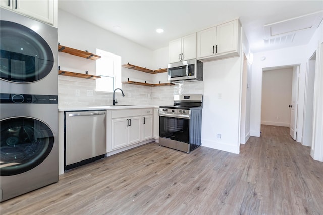 kitchen featuring white cabinets, stacked washer / drying machine, light hardwood / wood-style floors, and appliances with stainless steel finishes